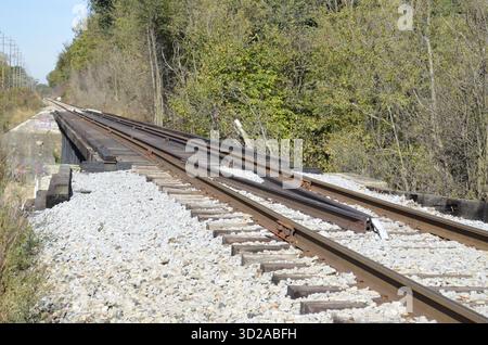 Verrostete Eisenbahnschienen mit zusätzlichen Schienen für Entgleisungsschutz und strukturelle Stabilität, wenn sie entlang einer Brücke über eine örtliche Straße oder Straße fahren. Stockfoto