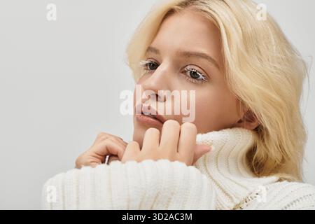 Eine schöne junge Frau mit weißen Wimpern lächelt sanft, während sie einen gemütlichen Strickpullover trägt. Stockfoto