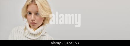Eine junge blonde Frau mit weißen Wimpern posiert in einem gemütlichen Strickpullover, Banner Stockfoto