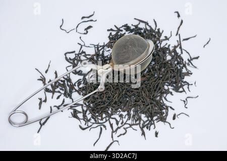 Schwarzer Tee mit losem Blatt und einem Tee-Infuser aus Edelstahl auf weißem Hintergrund. Konzepte der Teebrüherei, Bio-Getränke, gesunder Lebensstil und Natur Stockfoto