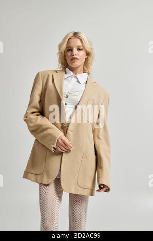 Eine schöne junge Frau steht selbstbewusst in einem modischen, beigefarbenen Outfit und zeigt Winterstil. Stockfoto