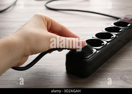Frau, die Stecker in die Steckdosenleiste am Holztisch steckt, Nahaufnahme Stockfoto