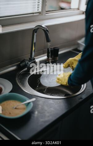 Nahaufnahme der Hände, die Geschirr in Küchenspüle unter fließendem Wasser waschen Stockfoto