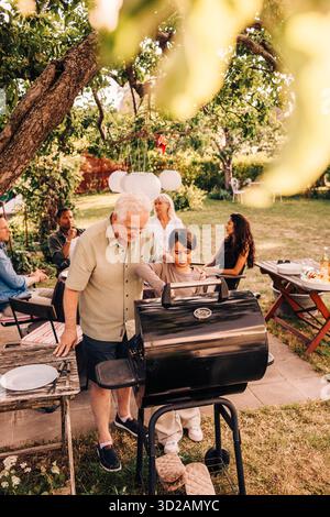 Blick auf den älteren Mann, der der Enkelin beim Barbecue auf der Gartenparty hilft Stockfoto