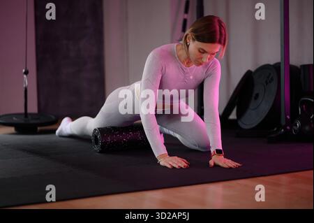 Attraktive Kurzhaarfrau in grauer Trainingsbekleidung mit Schaumstoffrolle auf einer Turnmatte. Stockfoto