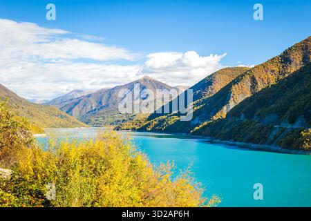 Malerischer Blick auf das türkisfarbene Zhinvali Reservoir in Georgia, umgeben von farbenfrohen Herbstwäldern und Berghängen unter einem klaren blauen Himmel. Friedliches Natu Stockfoto