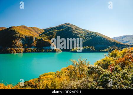 Malerischer Blick auf das Zhinvali Reservoir in Georgien, umgeben von farbenfrohen Herbstwäldern und Berghängen. Türkisfarbenes Wasser und klarer Himmel sorgen für ein Stockfoto