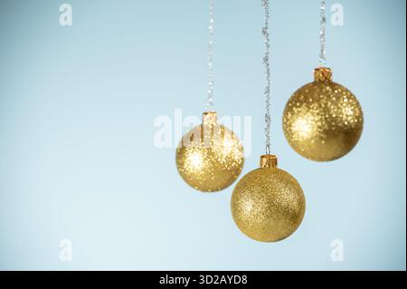 Drei goldene Weihnachtskugeln hängen auf blauem Hintergrund. Stockfoto