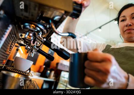 Blick aus einem niedrigen Winkel auf weibliche Barista, die Milch im Café aufschäumt Stockfoto