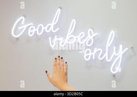 Ein Mädchen zeigt nach dem Besuch des Nagelsalons ihre gepflegten Hände und steht hinter dem weißen Neonschild mit der Aufschrift „Good Vibes Only“ Stockfoto