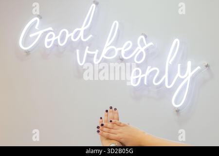 Ein Mädchen zeigt nach dem Besuch des Nagelsalons ihre gepflegten Hände und steht hinter dem weißen Neonschild mit der Aufschrift „Good Vibes Only“ Stockfoto