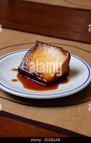 Traditionelles Flan- oder Crème-Karamell-Dessert mit reichhaltiger Sauce auf einem weißen Teller. Schwerpunkt auf klassischem süßem Genuss und gehobenem Essen. Stockfoto