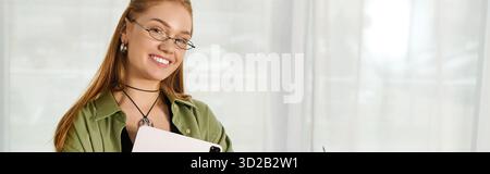 Gemütliche Heimszene mit einer jungen Frau, die ein Tablet hält und fröhlich lächelt. Stockfoto