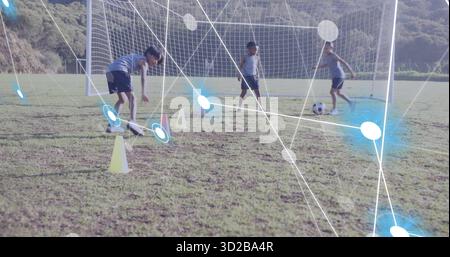 Drei Jungen beim Dribbeln von Fußball durch gelbe Kegel auf dem Spielfeld, durch Tornetz Stockfoto