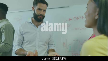 Mann mit Gesten, der im Sitzungssaal mit Bart spricht, mit Whiteboard, das Datendiagramme und Pfeile zeigt Stockfoto