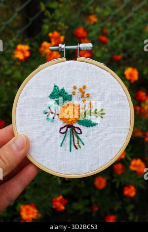 Nahaufnahme einer handgefertigten Blumenstickerei in einem hölzernen Ring mit gelbem und grünem Blumenmuster auf weißem Stoff. Stockfoto