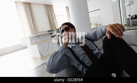 Ein erfolgreicher und selbstbewusster junger Geschäftsmann raucht in seiner idealen Wohnung, während er auf der Couch sitzt Stockfoto