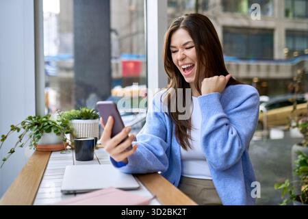 Junge, glückliche, aufgeregte Frau, die das Handy hält und den Sieg feiert. Stockfoto