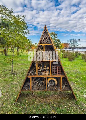 Große dreieckige Insekt-Hotelstruktur im Stadtpark in der Nähe des Sees mit natürlichen Materialien für die Biodiversität Stockfoto