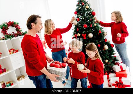 Die Familie versammelt sich um einen Weihnachtsbaum und schmückt mit Eltern und Kindern in roten Pullover Geschenke in einer warmen, festlichen Heimszene Stockfoto