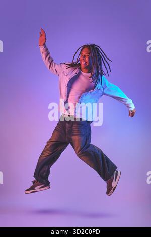 Energiegeladener glücklicher Mann mit Dreadlocks, der die Freiheit im Sprung feiert Stockfoto