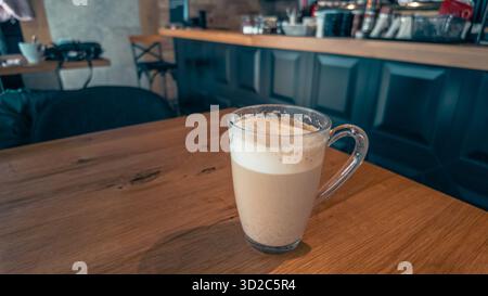 Glasbecher Kaffee auf Holztisch in der Nähe des Fensters im städtischen Café, Morgenlicht schafft warme Atmosphäre perfekt für Lifestyle- oder Geschäftskonzepte Stockfoto
