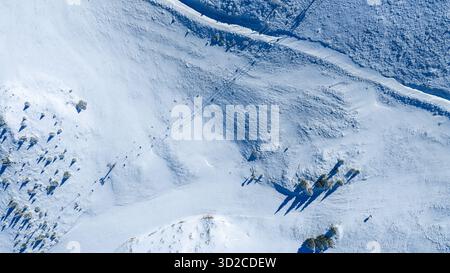 Aus der Vogelperspektive unberührte schneebedeckte Landschaft mit Schatten von Bäumen und Fußspuren durch gefrorenes Gelände Stockfoto
