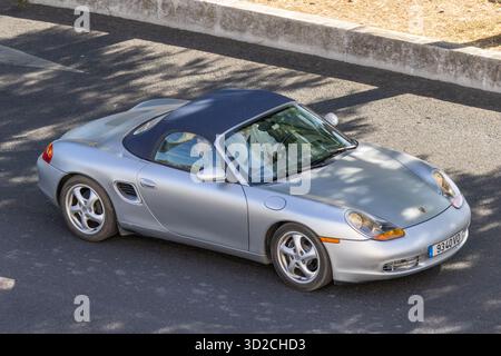 Silbernes porsche boxster Cabriolet, das auf einer Asphaltstraße mit Baumschatten fährt Stockfoto
