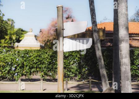 Leeres weißes Richtungsschild Modell auf Holzstange in sonnigem Park mit Grün und unscharfem Hintergrund, leere Pfeiltafeln Vorlage für Wegsuche oder Tram Stockfoto