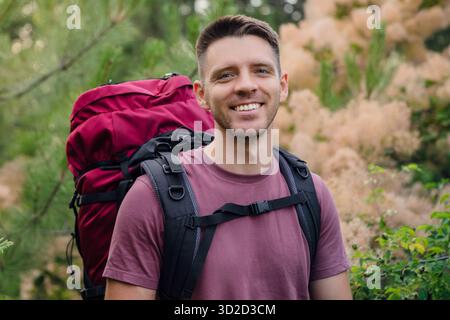 Lächelnder Rucksacktouristen im Wald während der Sommerwanderung. Outdoor-Reisen, Abenteuer und aktives Lifestyle-Konzept. Stockfoto