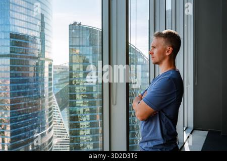 Ein junger Mann blickt aus dem Fenster auf Wolkenkratzer und Geschäftszentren Stockfoto