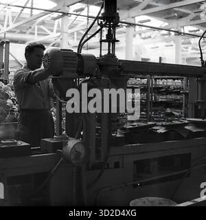 Archiv Schwarzweißfoto aus den 1970er Jahren in Sloviansk, Ukrainische SSR. Es zeigt einen männlichen Arbeiter, der eine große Industriemaschine im Armature-Isolator Plant (AIZ) bedient. Er steht an seinem Arbeitsplatz und konzentriert sich darauf, ein Bauteil, möglicherweise einen Elektromotor, an der komplexen Maschine anzupassen. Im Vordergrund ist ein Manometer zu sehen. Der Hintergrund zeigt den Innenraum der Werkstatt. Dieses Bild ist ein klassisches Beispiel für einen sowjetischen Industriearbeiter, der in der Produktion tätig ist Stockfoto