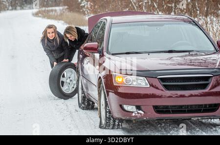 Buchse mit Wechselrad. Frauen wechseln im Winter den beschädigten Reifen an seinem Auto. Mädchen ersetzt Reifen. Störwagen im Winter Stockfoto