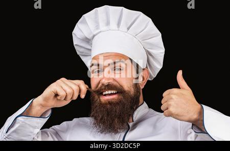 Bärtige Köche, Köche oder Bäcker positive Geste mit der Hand, Daumen hoch lächelnd und glücklich für den Erfolg. Glücklicher Koch, junger Mann mit Bart, der Daumen zeigt Stockfoto