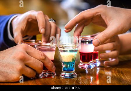 Leute trinken beim Aperitif. Mehrere Alkoholgläser. Schüsse auf einer Bartheke. Set mit Cocktails. Männliche Hände jubeln mit Wodka Stockfoto