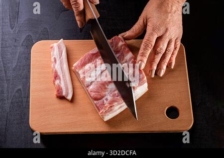 Ein Koch schneidet Schmalzfleisch ein Messer in einem Restaurant. Metzgerhände aus nächster Nähe: Fleisch schneiden. Stück Rohschmalz. Der Metzger schneidet das Fleisch roh frisches Schweinefleisch auf Stockfoto