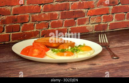 Rührei mit grünen Zwiebeln, gebratenen Tomaten und Brotcroutons auf einem Holztisch, eine Gabel in der Nähe. Nahaufnahme. Stockfoto