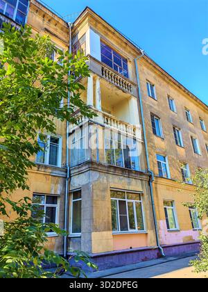Altes gelbes Wohngebäude mit abgenutzten Balkonen und dekorativen Säulen, die Anzeichen von Putzschäden und Witterungseinflüssen zeigen. Das Foto hebt die Fassade hervor Stockfoto