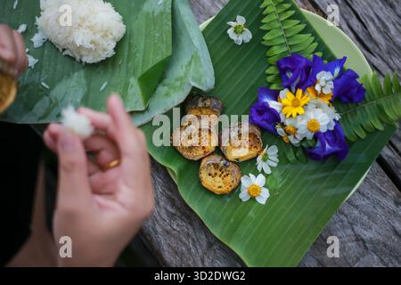 Selektiver Fokus Ricefield-Krabben in ihren Muscheln. Sehen Sie Na beim Essen zu und dekorieren Sie den Teller mit natürlichen Blumen. Essen Sie mit klebrigem Reis, der in Bananenlaub gewickelt ist Stockfoto