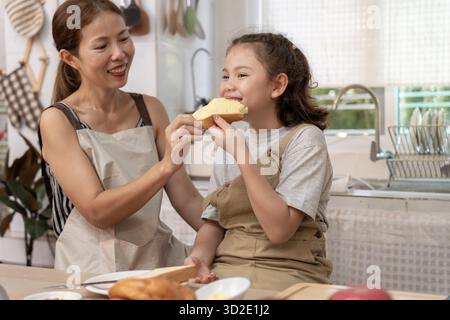 Gemeinsame Aktivitäten während der Feiertage. Eltern und Kinder essen zusammen, Mutter bereitet das Frühstück für die Tochter am Morgen vor, genießen Sie, kleine Stockfoto