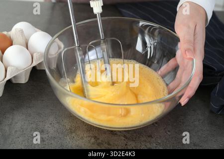 Frau, die Eier mit Mixer am grauen Tisch schlägt, Nahaufnahme Stockfoto