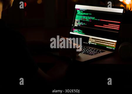 Die Hände des Programmierers programmieren auf einem Laptop im Dunkeln mit Blick auf die Lichter der Nachtstadt. Das Konzept eines Entwicklers oder Hackers. Stockfoto