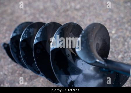 Nahaufnahme des nassen Stahlschneckenbohrers mit sauberen Spiralklingen mit Wassertröpfchen nach dem Hochdruckwaschen, für Bodenbohrungen, Fundamentbau Stockfoto