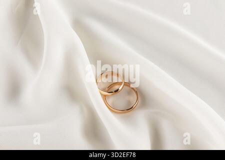 Zwei goldene Eheringe liegen auf weichen Falten aus elegantem Seidenstoff. Wunderschönes Hochzeitsdesign. Eine Kopie des Bereichs. Hochzeitshintergrund Stockfoto