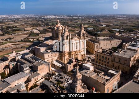 Aus der Vogelperspektive von Mdina, Malta, zeigt St. Paul's Cathedral, honigfarbenen Kalkstein, enge Gassen und Bastionsmauer mit ländlichen Feldern und Küste in b Stockfoto