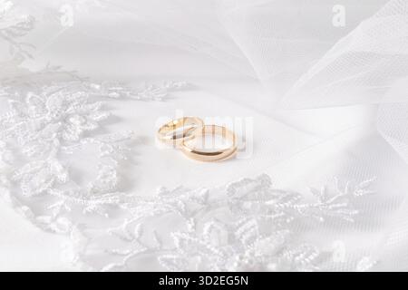 Zwei goldene Eheringe liegen auf dem gestickten Tüll der Braut mit weichen Falten. Wunderschöner Hochzeitshintergrund. Layout für Design. Eine Postkarte Stockfoto