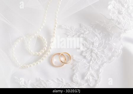 Hochzeitshintergrund mit schickem weißem Spitzenteil am Schleier der Braut und zwei goldenen Eheringen darauf. Weiße Perlen. Layout der Einladungen Stockfoto