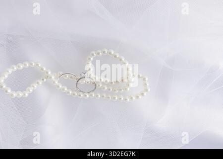 Ein schicker Hintergrund für Hochzeitsdesign. Eine elegante weiße Perlenkette und zwei weiße goldene Verlobungsringe Stockfoto
