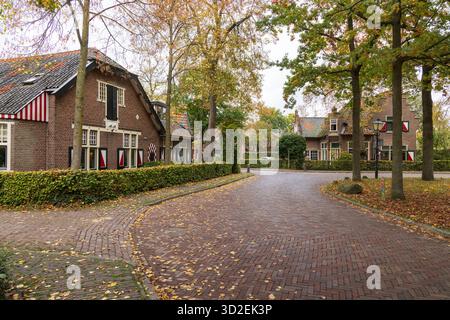 Charmante Kopfsteinpflasterstraße mit traditionellen niederländischen Backsteinhäusern und Herbstbäumen im Dorf Haarzuilens, Niederlande. Stockfoto