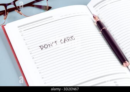 Ein offener Tagesplaner mit den Worten „Don t Care“ auf der Seite. In der Nähe der Bindung liegt ein Stift auf, und die Brille sitzt in der linken oberen Ecke Stockfoto